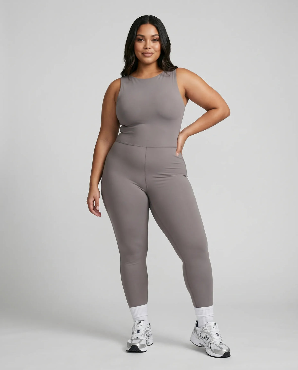 Model standing front-on in a studio wearing the purple backless flare bodysuit with white sneakers.