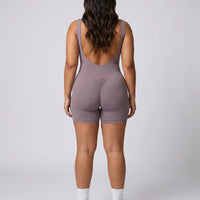 Model facing away in a studio showing the open back detail of the purple flare bodysuit.