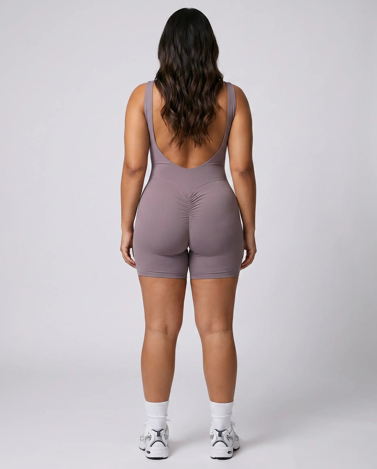 Model facing away in a studio showing the open back detail of the purple flare bodysuit.