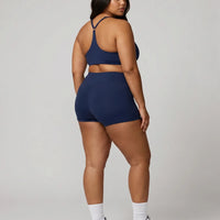 Model wearing the blue sculpting sports bra top, back view showing strap layout in a studio setting.