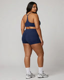 Model wearing the blue sculpting sports bra top, back view showing strap layout in a studio setting.