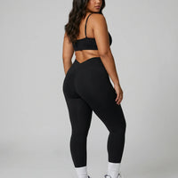 Model standing with her back to camera in a studio wearing a black V-neck bra top showing rear strap layout.
