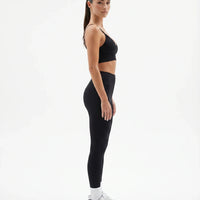 Plus size model facing front in a studio wearing a black compression bra top with a sculpting V-neckline.