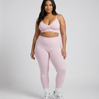 Model wearing pink ribbed bra top and matching leggings, front studio shot on neutral background.