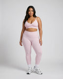 Model wearing pink ribbed bra top and matching leggings, front studio shot on neutral background.