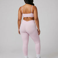 Model wearing pink ribbed bra top and matching leggings, rear studio view showing back coverage and strap placement.