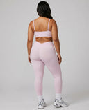 Model wearing pink ribbed bra top and matching leggings, rear studio view showing back coverage and strap placement.