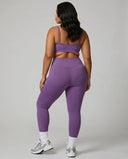 Model facing away in studio showing the back fit of the purple seamless bra top and high waist legging set.