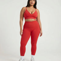 Female model facing forward in studio wearing red ribbed seamless bra top paired with matching red leggings and white sneakers.