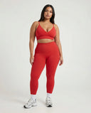 Female model facing forward in studio wearing red ribbed seamless bra top paired with matching red leggings and white sneakers.