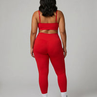 Female model facing away in studio showing the back fit of the red ribbed seamless bra top and matching leggings.