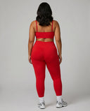 Female model facing away in studio showing the back fit of the red ribbed seamless bra top and matching leggings.