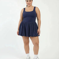 Female model standing front-on in a studio wearing the SEEN Essential balloon hem dress in badge blue with white sneakers and a headband.