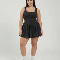 Model facing forward wearing black balloon activewear dress with white sneakers in a studio setting.