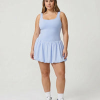 Model standing front-on in studio wearing light blue balloon hem activewear dress with white sneakers and headband.