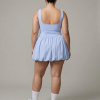 Model posing from behind in studio wearing light blue balloon hem dress showing back silhouette and skirt volume.