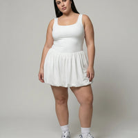 Model wearing white balloon hem active dress in a front-facing studio shot with sneakers and headband.