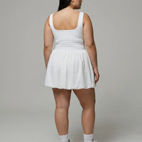 Model wearing white balloon hem active dress from behind in a clean studio setting.