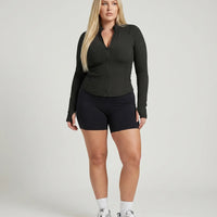 Female model facing front in studio wearing black sculpting zip-up jacket with bike shorts and sneakers.