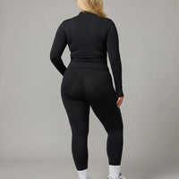 Female model from behind in studio wearing black long sleeve zip-up activewear jacket paired with bike shorts.