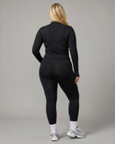 Female model from behind in studio wearing black long sleeve zip-up activewear jacket paired with bike shorts.