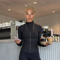 Plus size model front view wearing black ribbed zip-up jacket styled with bike shorts in a studio setting.