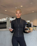 Plus size model front view wearing black ribbed zip-up jacket styled with bike shorts in a studio setting.