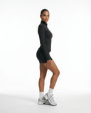 Lifestyle image of woman wearing black sculpting zip-up jacket walking outdoors with a relaxed athleisure look.