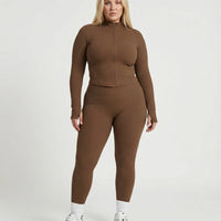 Female model facing forward in studio wearing brown ribbed sculpting zip jacket paired with matching brown leggings.