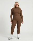 Female model facing forward in studio wearing brown ribbed sculpting zip jacket paired with matching brown leggings.