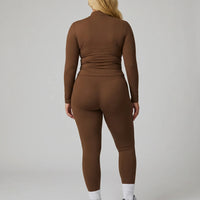 Female model facing away in studio showing the back fit of the brown ribbed zip jacket and matching leggings.
