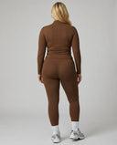 Female model facing away in studio showing the back fit of the brown ribbed zip jacket and matching leggings.