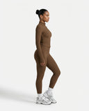 Lifestyle shot of woman wearing brown ribbed zip jacket outdoors walking with confidence in an athleisure setting.