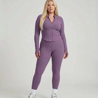 Model standing front-on in studio wearing purple sculpting ribbed zip jacket and matching high waist leggings.