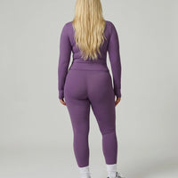 Model facing away in studio showing the back fit of the purple ribbed jacket and legging activewear set.