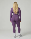 Model facing away in studio showing the back fit of the purple ribbed jacket and legging activewear set.