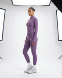 Lifestyle shot of woman wearing purple ribbed zip jacket and legging set walking outdoors in natural light.