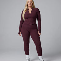 Model facing forward in wine red zip-up jacket top and matching leggings in a bright studio setting.