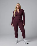 Model facing forward in wine red zip-up jacket top and matching leggings in a bright studio setting.