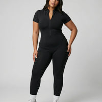 Model standing front-on in studio wearing brown sculpting jumpsuit legging with short sleeves and front zip closure.