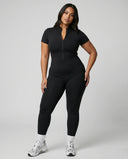 Model standing front-on in studio wearing brown sculpting jumpsuit legging with short sleeves and front zip closure.