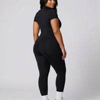 Model standing with back to camera in studio showing the rear fit of the brown jumpsuit legging from neckline to ankle.
