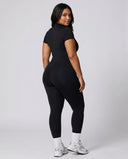 Model standing with back to camera in studio showing the rear fit of the brown jumpsuit legging from neckline to ankle.