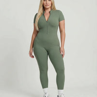 Female model facing forward wearing green ribbed sculpting jumpsuit in studio with neutral background.