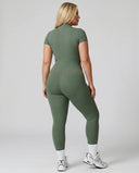 Female model from behind wearing green ribbed half-zip jumpsuit showing back fit in studio setting.