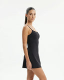 Lifestyle image of woman wearing black padel dress with built-in shorts during an active padel session on court.