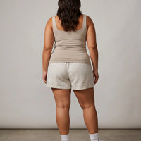 Model wearing beige sleeveless tank top photographed from behind in studio lighting.