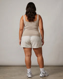 Model wearing beige sleeveless tank top photographed from behind in studio lighting.