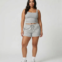 Female model standing front-on in studio wearing gray square-neck sleeveless tank top with gray shorts and white sneakers.