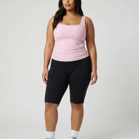 Female model facing forward in a studio wearing a pink square neck sleeveless tank top with black leggings.